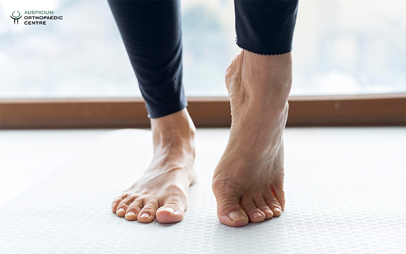 Close-up of feet on a white mat indoors, one foot flat and the other raised on toes in a stretch.