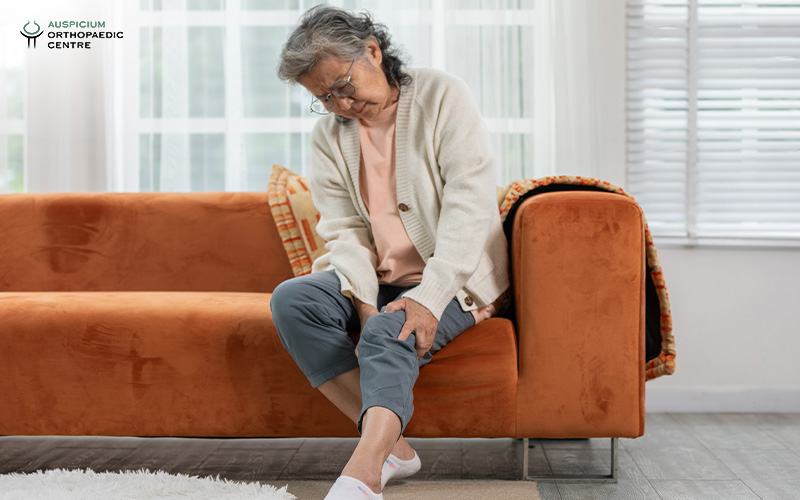 Elderly woman holding her painful knee on a couch.