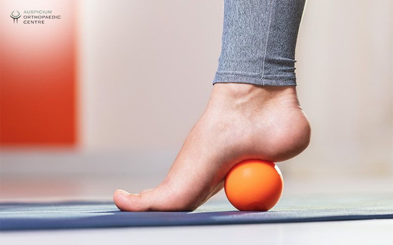 Foot rolling on an orange massage ball for heel pain.