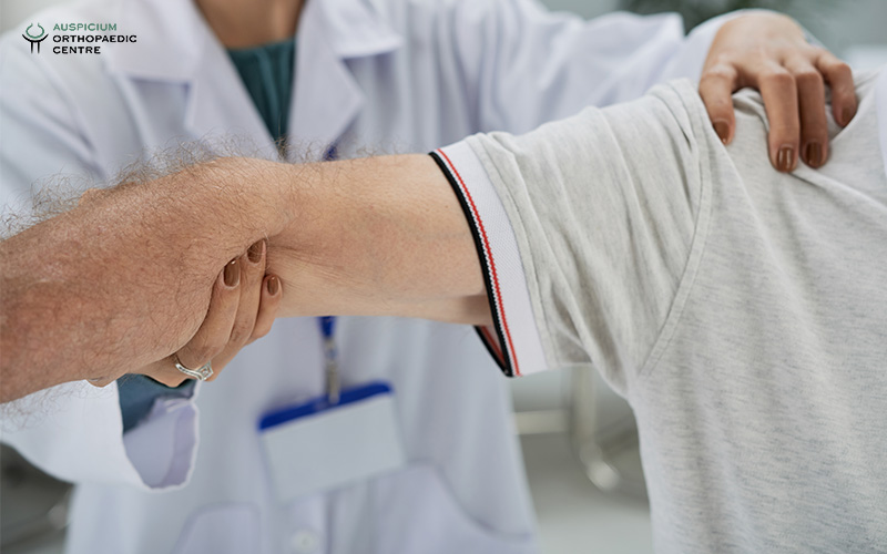 Medical professional in white coat supporting a patient's arm during an orthopedic exam in a clinic.