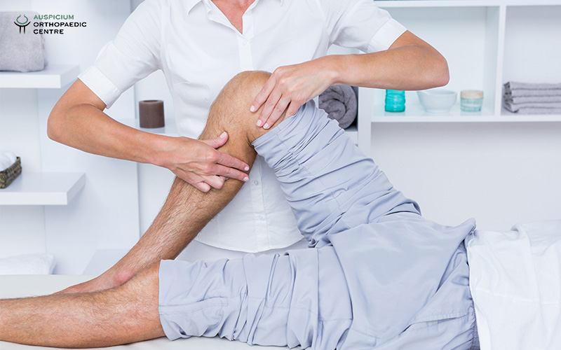 Medical professional in white uniform performing leg therapy on a patient lying on an exam table in clinic.
